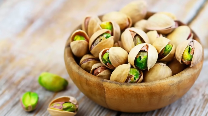 কাঠের টেবিলে রাখা এক বাটি তাজা পেস্তা বাদাম